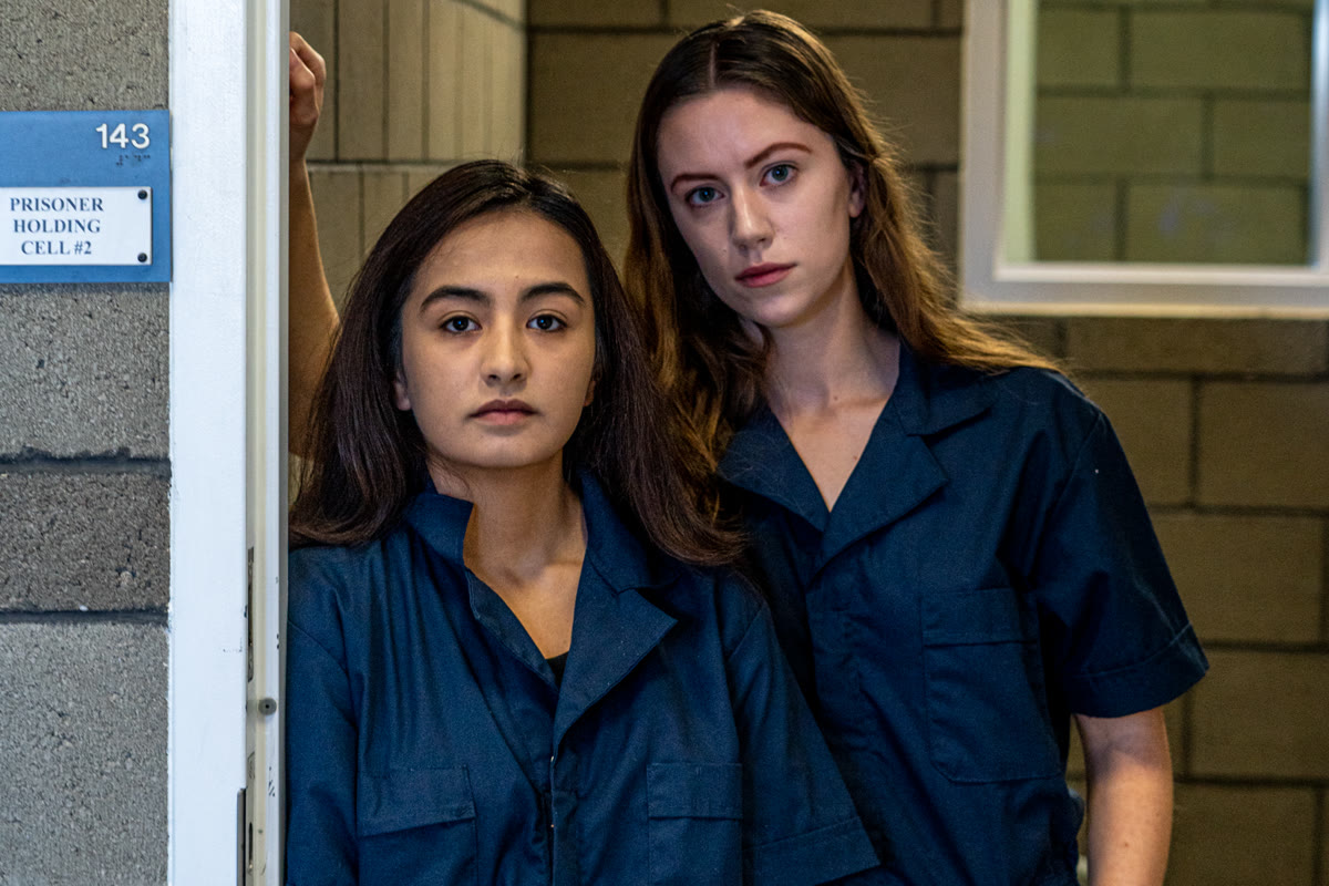 Still from Sleepovers: two teen girls in navy jumpsuits stand in a doorway