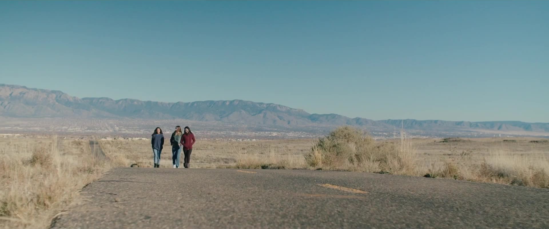 Three teen girls walk together across open desert
